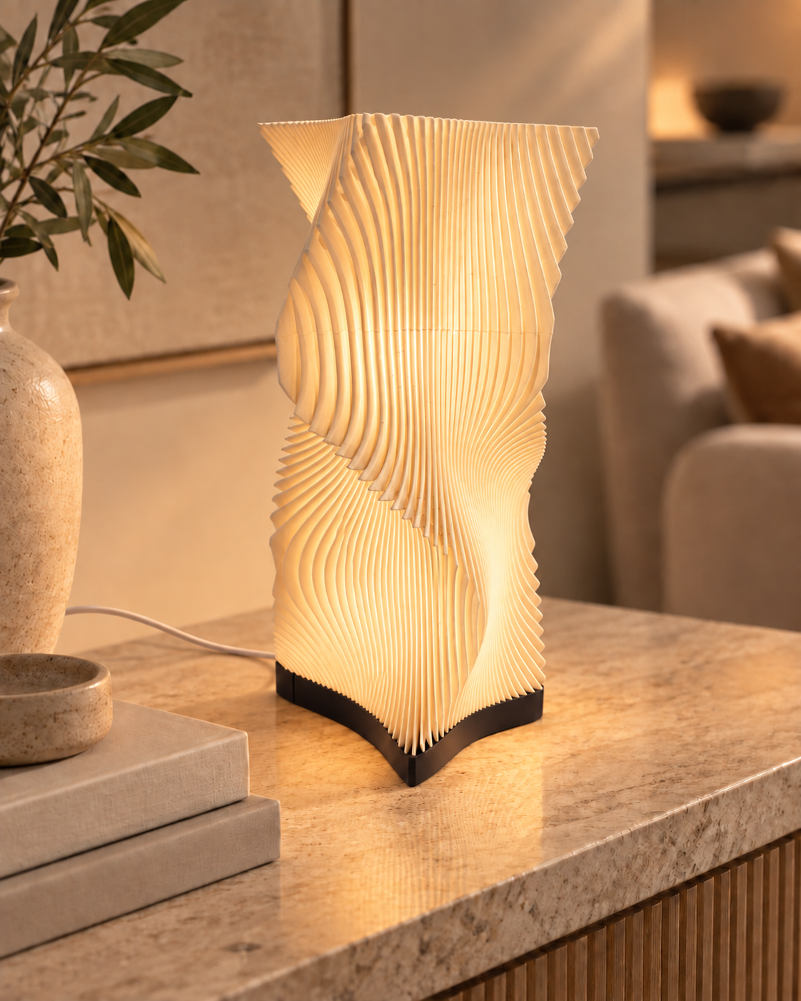 Vela sculptural table lamp illuminated with warm ambient light on a stone side table